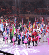 People standing and holding flags in a gymnasium during FADAM opening ceremony